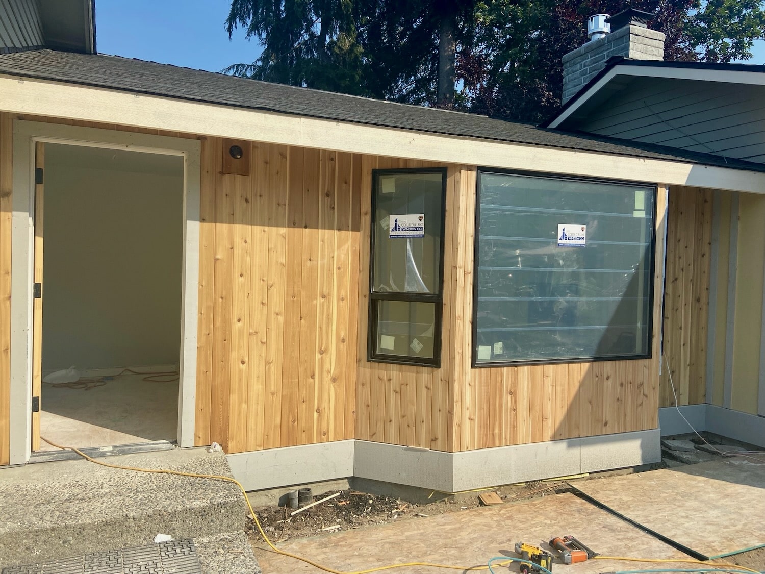 Fresh unfinished vertical cedar siding and new white trim fitted around black-framed windows on a Seattle ranch home